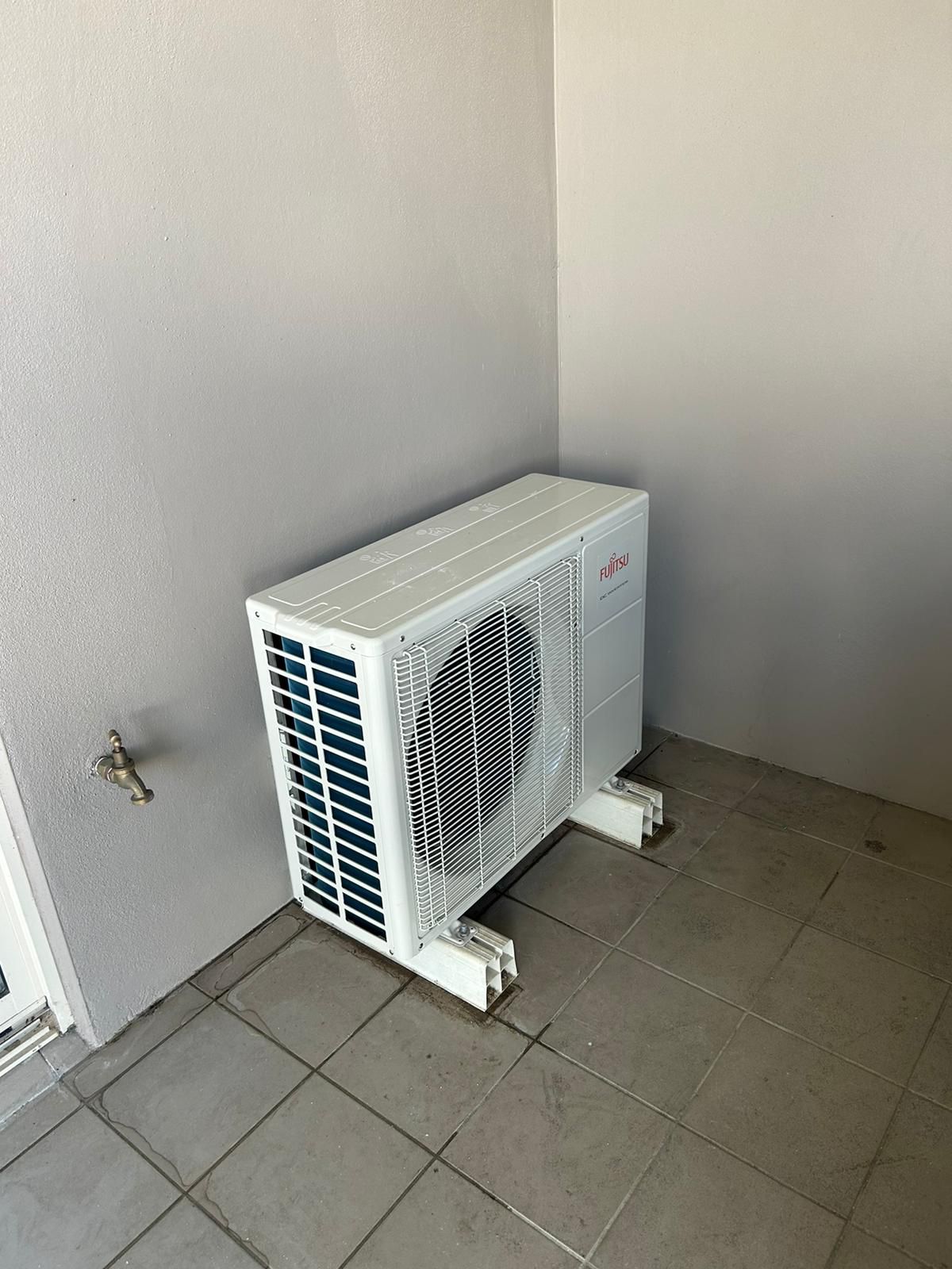 Fujitsu outdoor unit neatly installed on raised feet in tiled courtyard corner