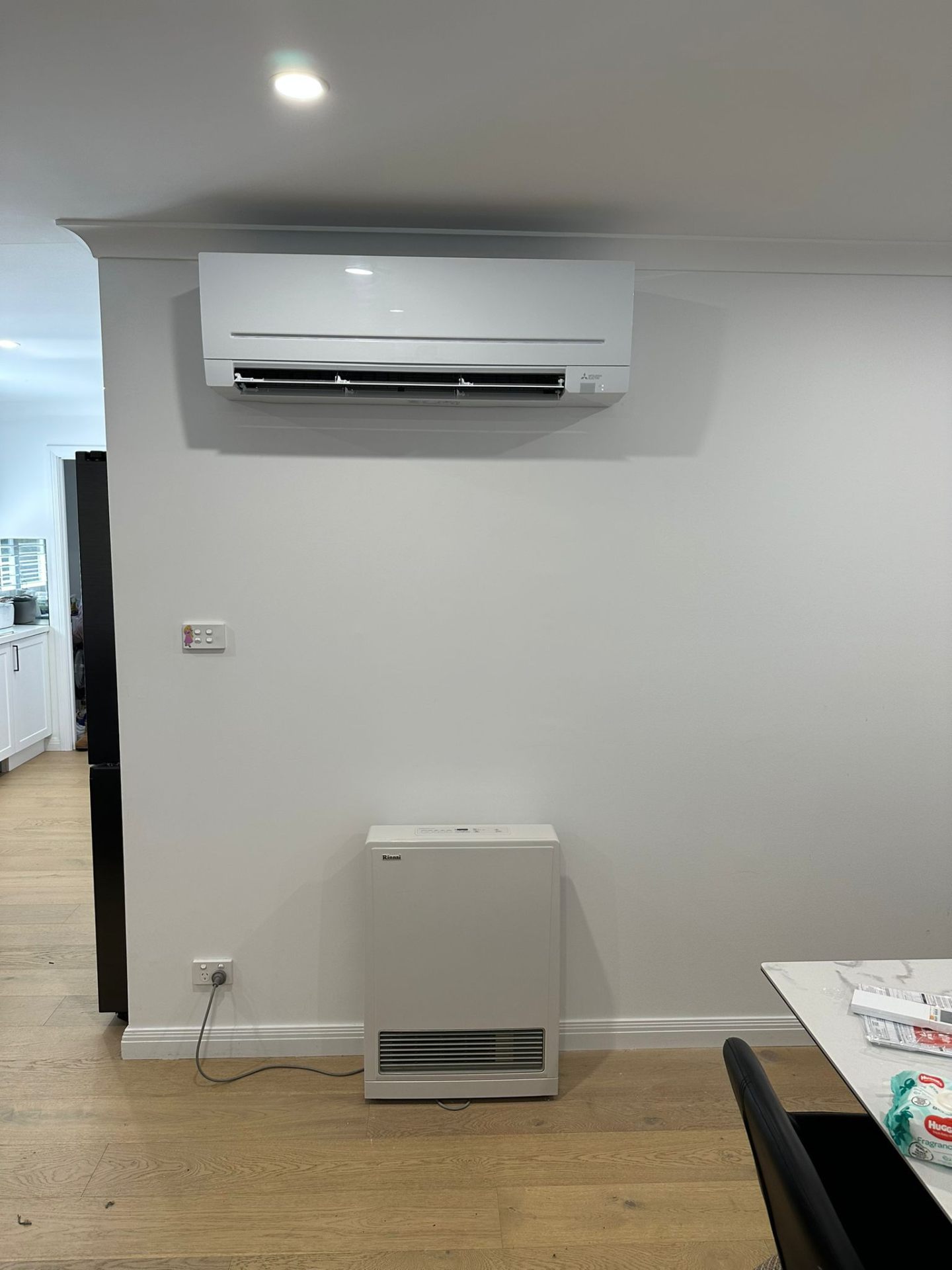 Mitsubishi indoor split system mounted high on living room wall above gas heater