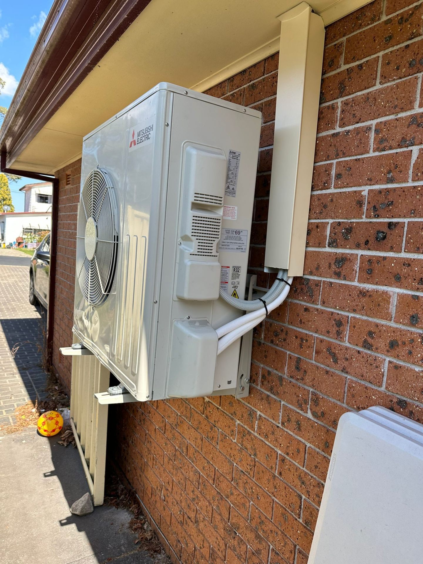 Mitsubishi Electric outdoor unit wall-bracketed on red brick home with tidy conduit downpipe