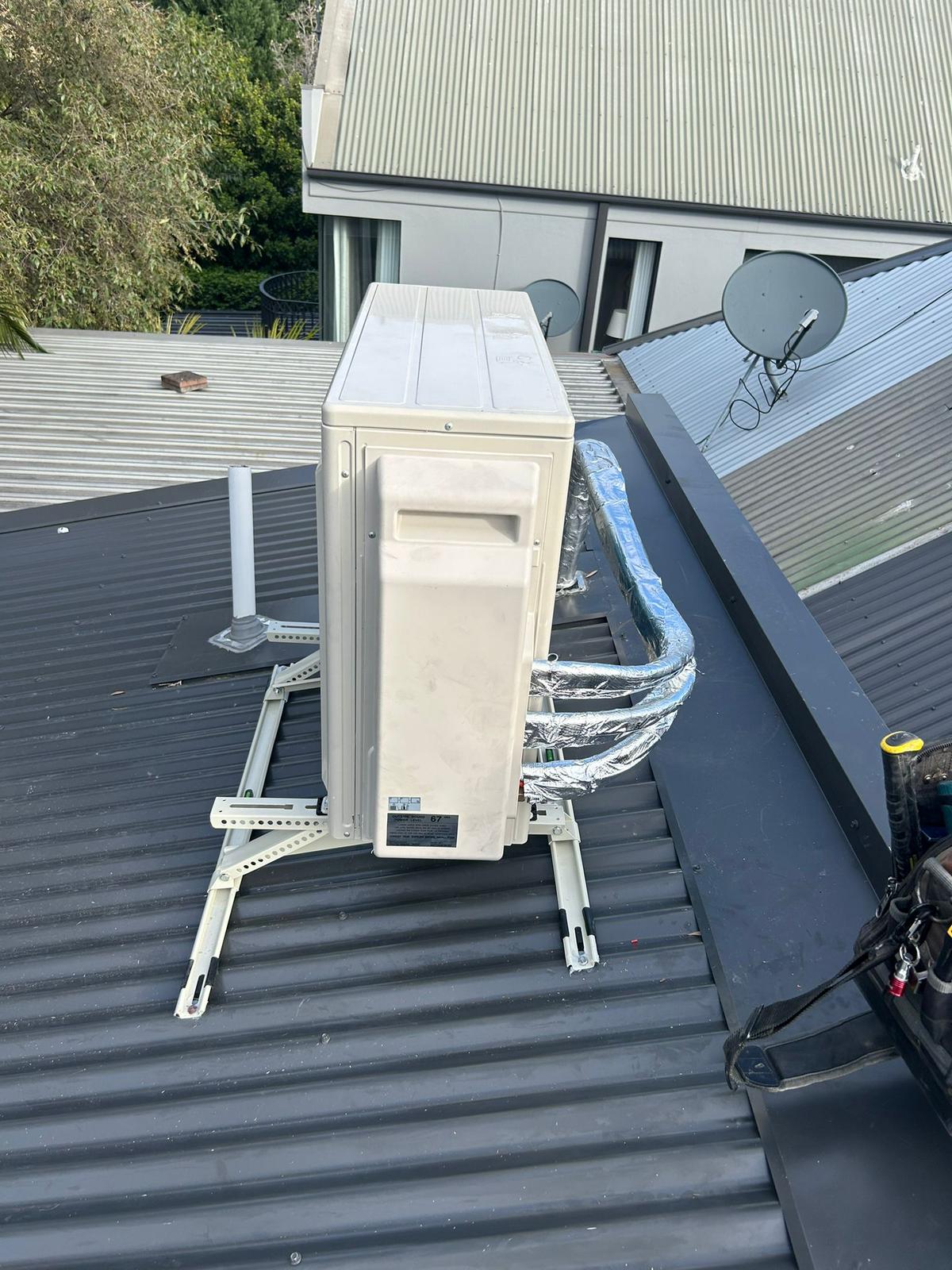 Outdoor air conditioning unit mounted on roof brackets above colorbond roofing