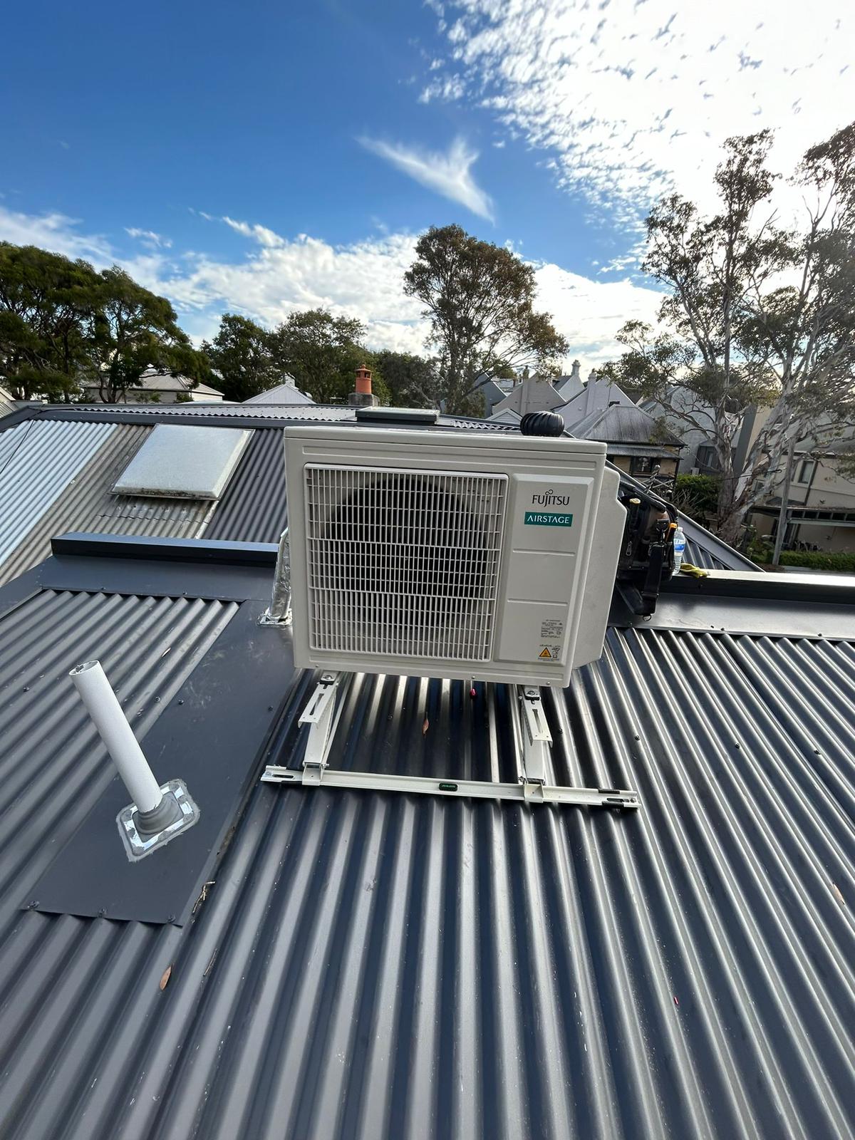 Fujitsu Airstage outdoor unit installed on rooftop frame with city skyline behind