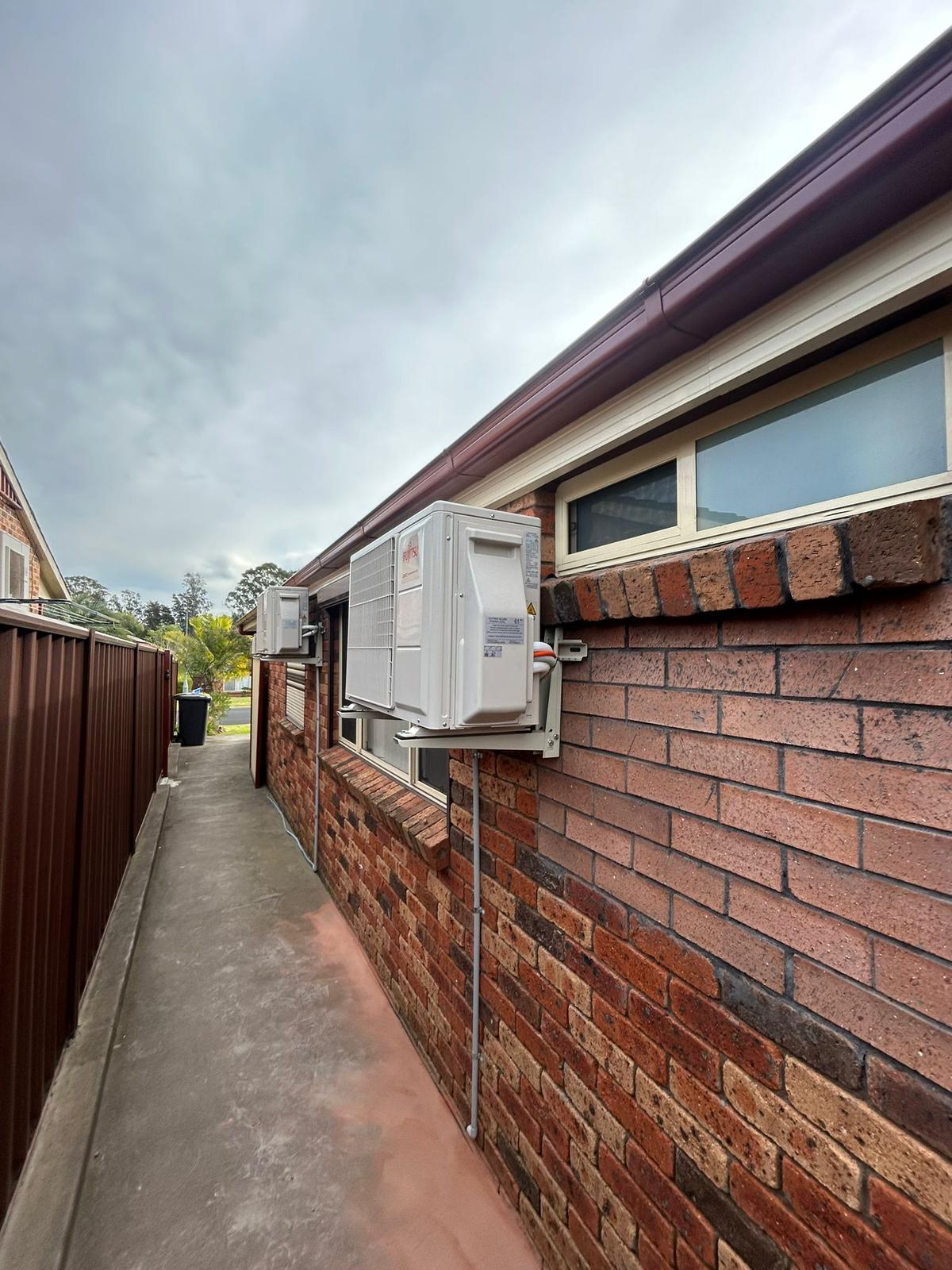 Fujitsu outdoor units installed on side passage of red brick home with neat conduit